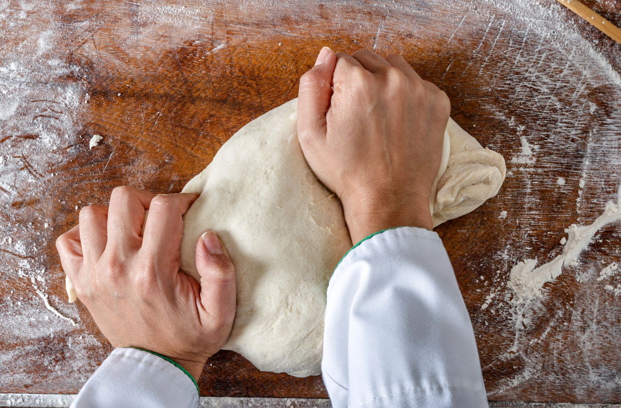 Las manos de una persona amasando una masa de pan encima de una superficie con harina