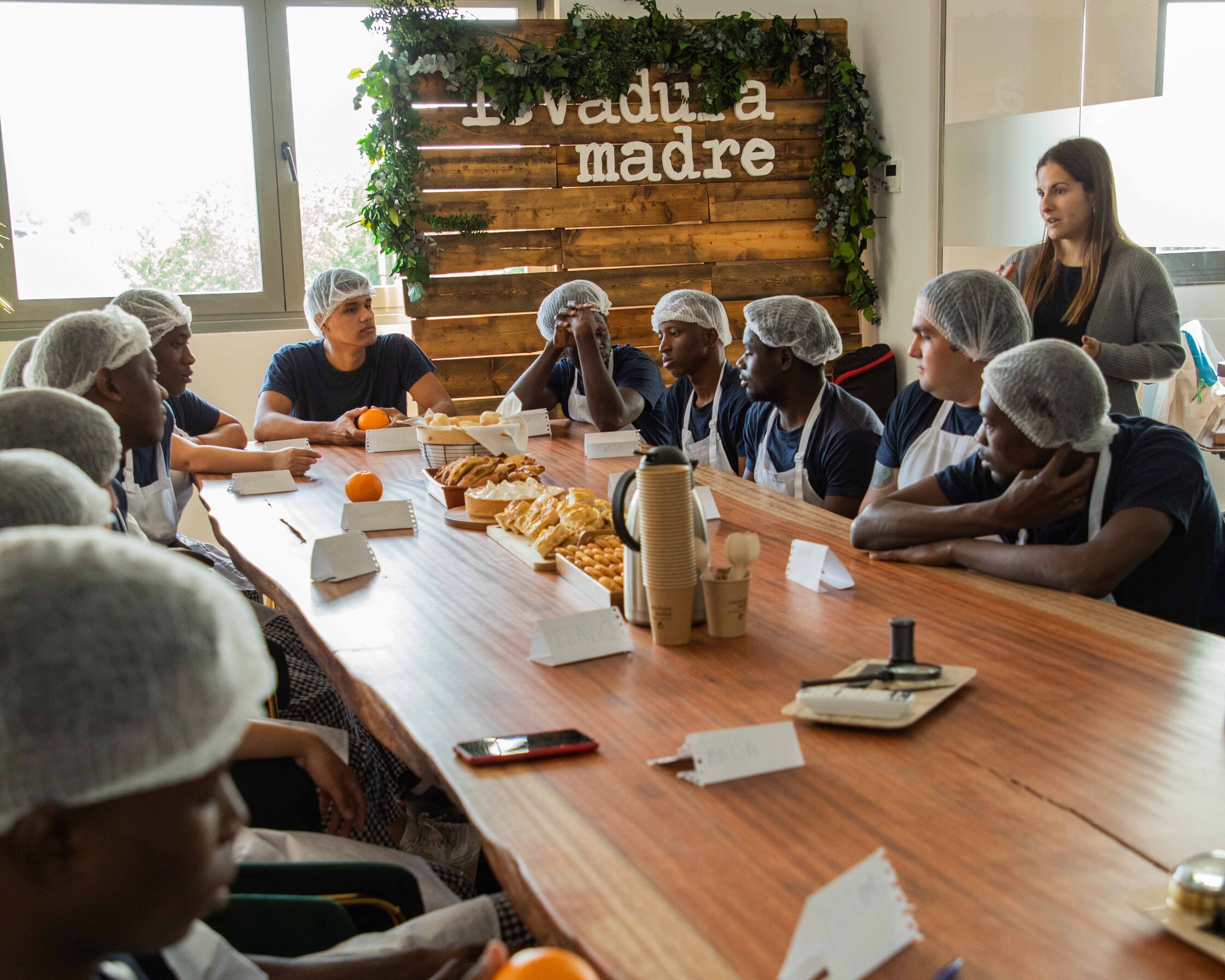 Un grupo de jóvenes vestidos con delantal de panaderos alrededor de una mesa con productos de repostería