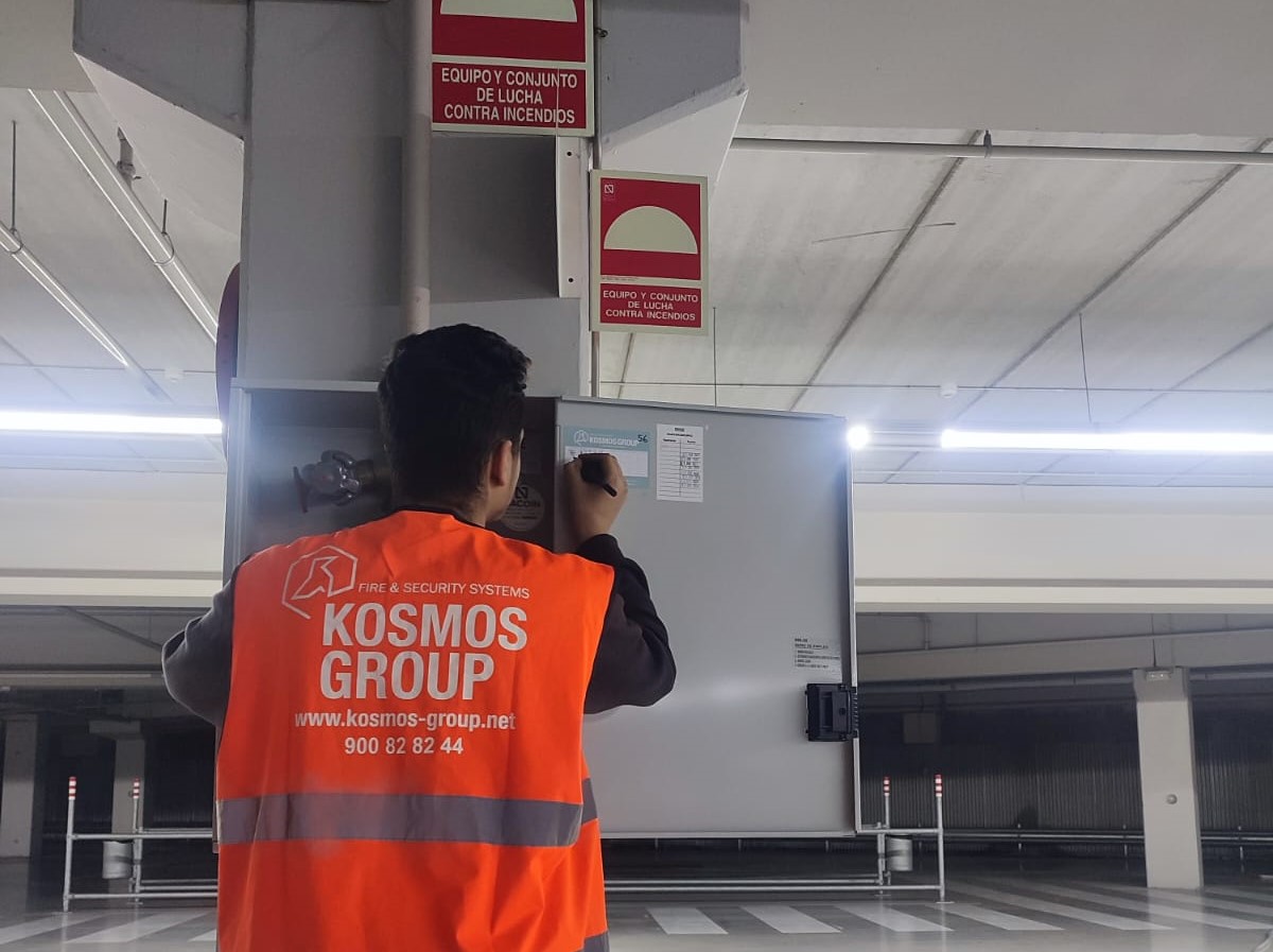 Un chico de espaldas con un chaleco de Kosmos Group escribiendo en una ficha pegada en un cuadro de mandos