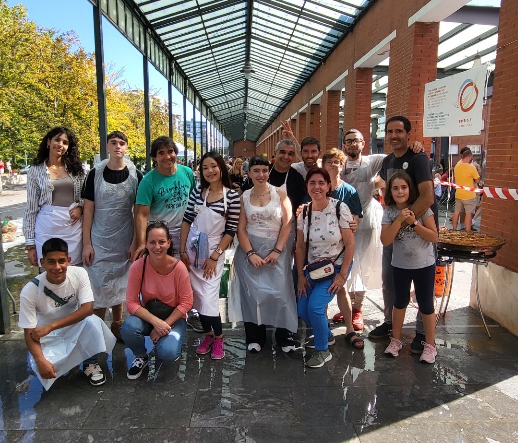 Un grupo de jóvenes vestidos con delantal posando con una paella 