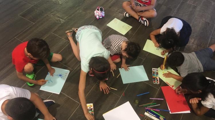 foto cenital de un grupo de niños y niñas dibujando con papeles en el suelo