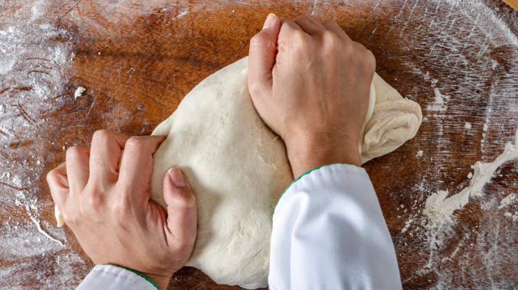 Las manos de una persona amasando una masa de pan encima de una superficie con harina