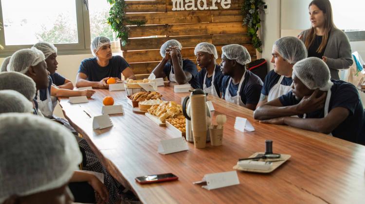 Un grupo de jóvenes vestidos con delantal de panaderos alrededor de una mesa con productos de repostería