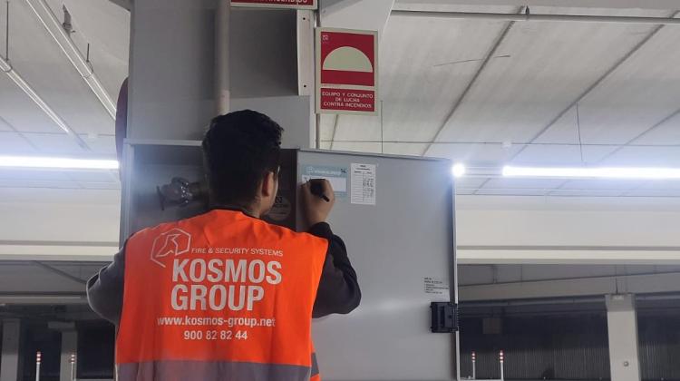 Un chico de espaldas con un chaleco de Kosmos Group escribiendo en una ficha pegada en un cuadro de mandos