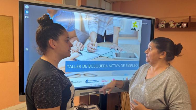 Dos mujeres hablando. De fondo una pantalla en la que se lee: Taller de búsqueda activa de empleo