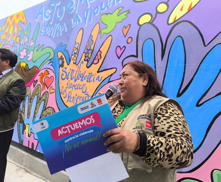 Una persona hablando con un micrófono. en la mano un cartel que lee: Actuamos contra la violencia ¡No es normal!