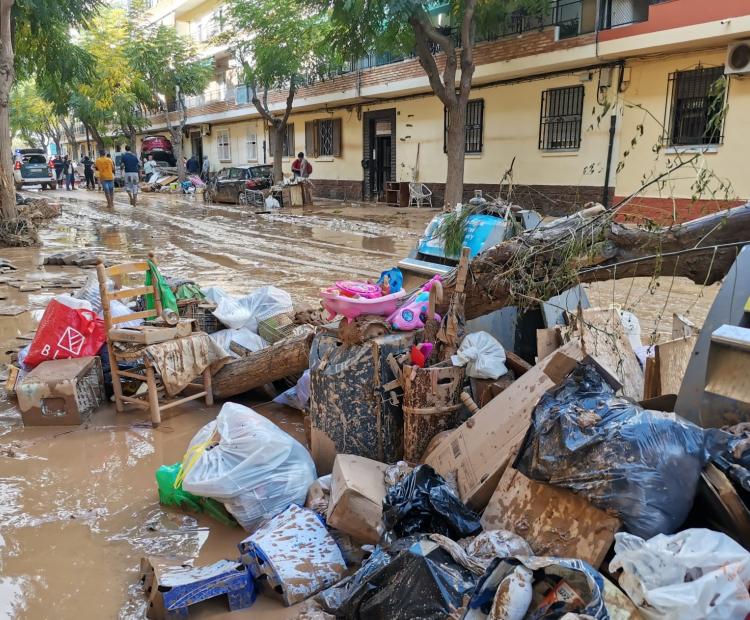 Imagen de una calle de casa bajas con el pavimento cubierto de barro y en primer plano una pila de basura y escombros también con barro