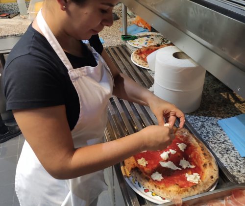 Una chica poniendo ingredientes encima de una masa de pizza