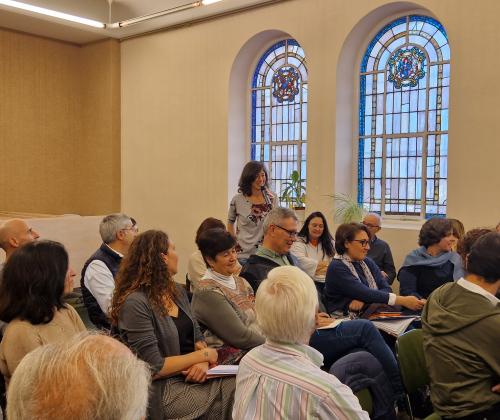 Público sentado en las sillas de una sala de actos y una persona de pie con un micrófono