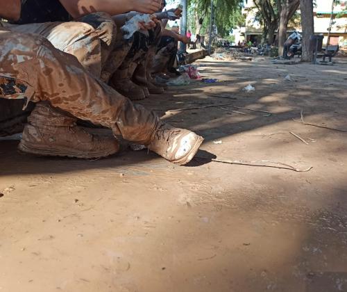 Imagen de personas sentadas con las botas llenas de barro. La calle al fondo también se ve llena de barro