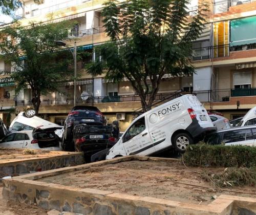 Una calle con edificios residenciales al fondo. En primer plano se ven coches apilados encima de otros y cubiertos de barro